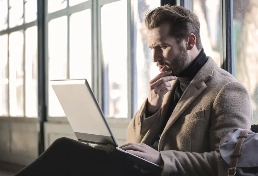 decor - a man holding his chin, wondering in a corporate office environment with a laptop on his lap